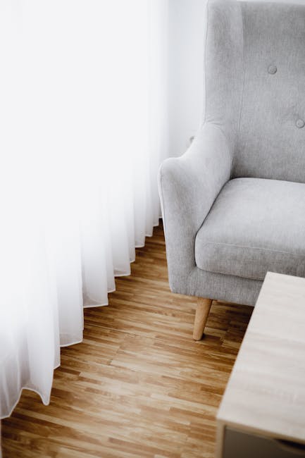 A mustard yellow upholstered armchair with a cushioned backrest and armrests, situated on a caster wheel base on a concrete floor against a plain white wall. The chair appears clean, with smooth fabric, and the area around is minimalistic without additional objects or decorations. This setting illustrates a simple domestic or commercial environment emphasizing surface cleanliness, which is relevant to proper upholstery surface cleaning and maintenance. For effective deep cleaning and sanitisation of similar furniture, Carpet Cleaning Harringay offers professional services to avoid common upholstery cleaning mistakes made by landlords. The overall scene highlights the importance of regular cleaning to maintain hygiene and prolong furniture life.