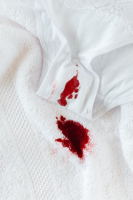 Close-up image of a white cloth wiping away fresh red wine spill stains on a smooth pink surface, likely a table or countertop. Visible red wine stains are scattered, with some streaks and droplets, indicating a recent spill. The white cloth is partially folded and positioned over part of the stain, suggesting an active cleaning process aimed at stain removal. The surface appears clean apart from the spill, and the lighting highlights the contrast between the red wine stains and the pink surface. This image relates to surface cleaning and stain removal services, as provided by Carpet Cleaning Harringay, emphasizing quick and effective domestic cleaning solutions.